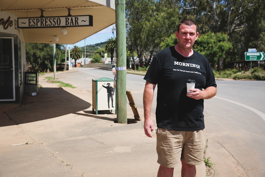 A man standing in front of a cafe with a coffee in his hand. 