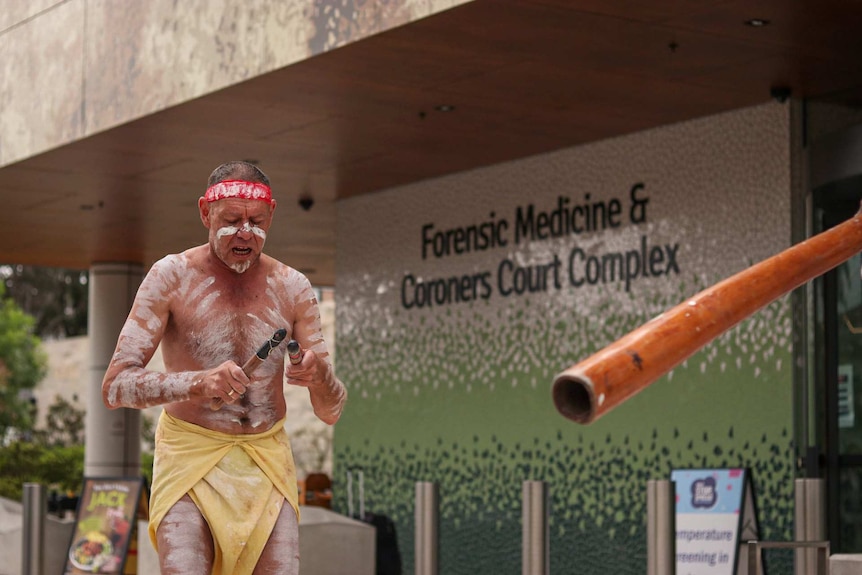 An Indigenous man with body painting plays clapping sticks