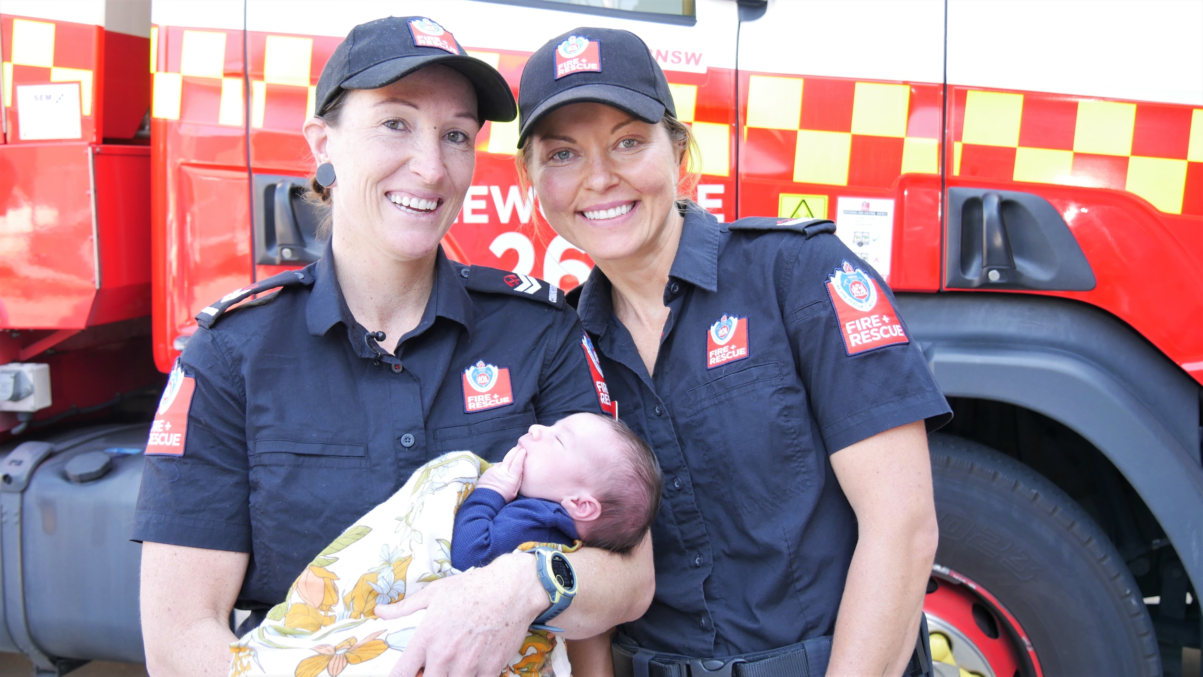 Sam and Liz holding baby Andy in front of a fire truck 