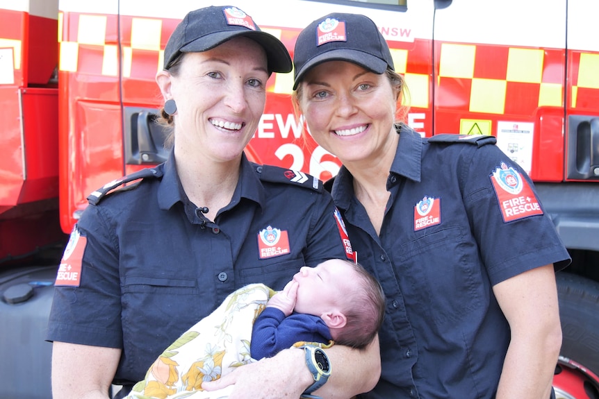 Sam and Liz holding baby Andy in front of a fire truck 