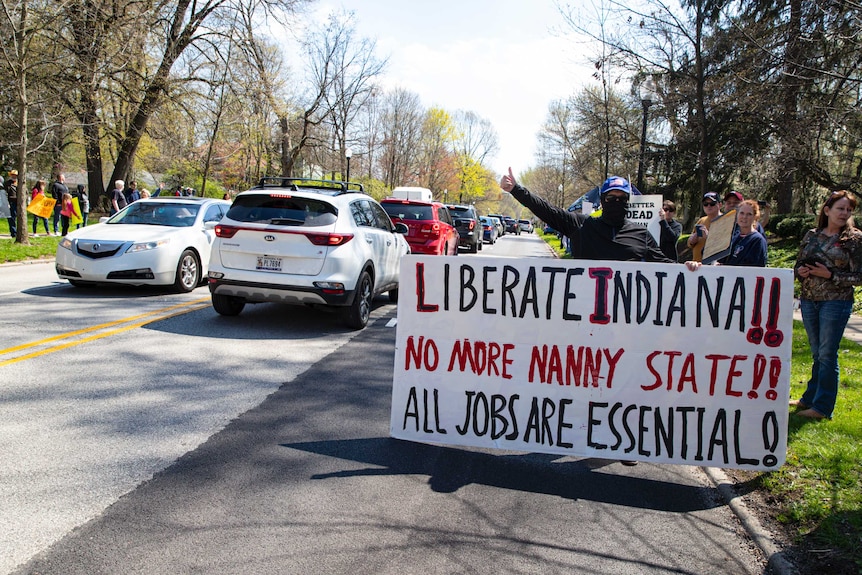 A protestor holds up his thumb while gripping a sign saying 'liberate Indiana'