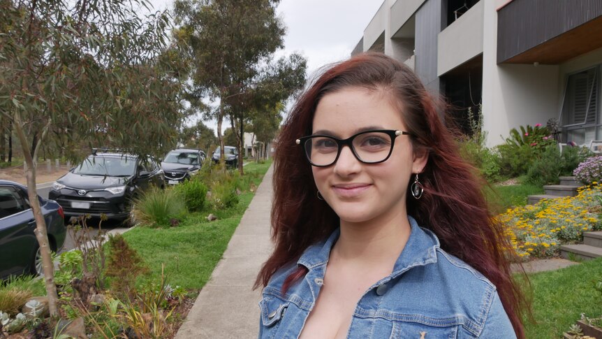 Girl with glasses, standing outside, smiling.