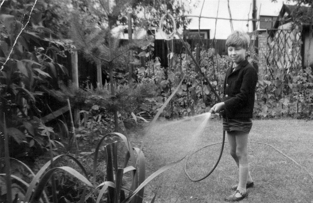 Black-and-white photo of Jerry Coleby-Williams as a child, watering a backyard