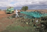 A man wearing a white suit sprays blue glue over a pile of waste
