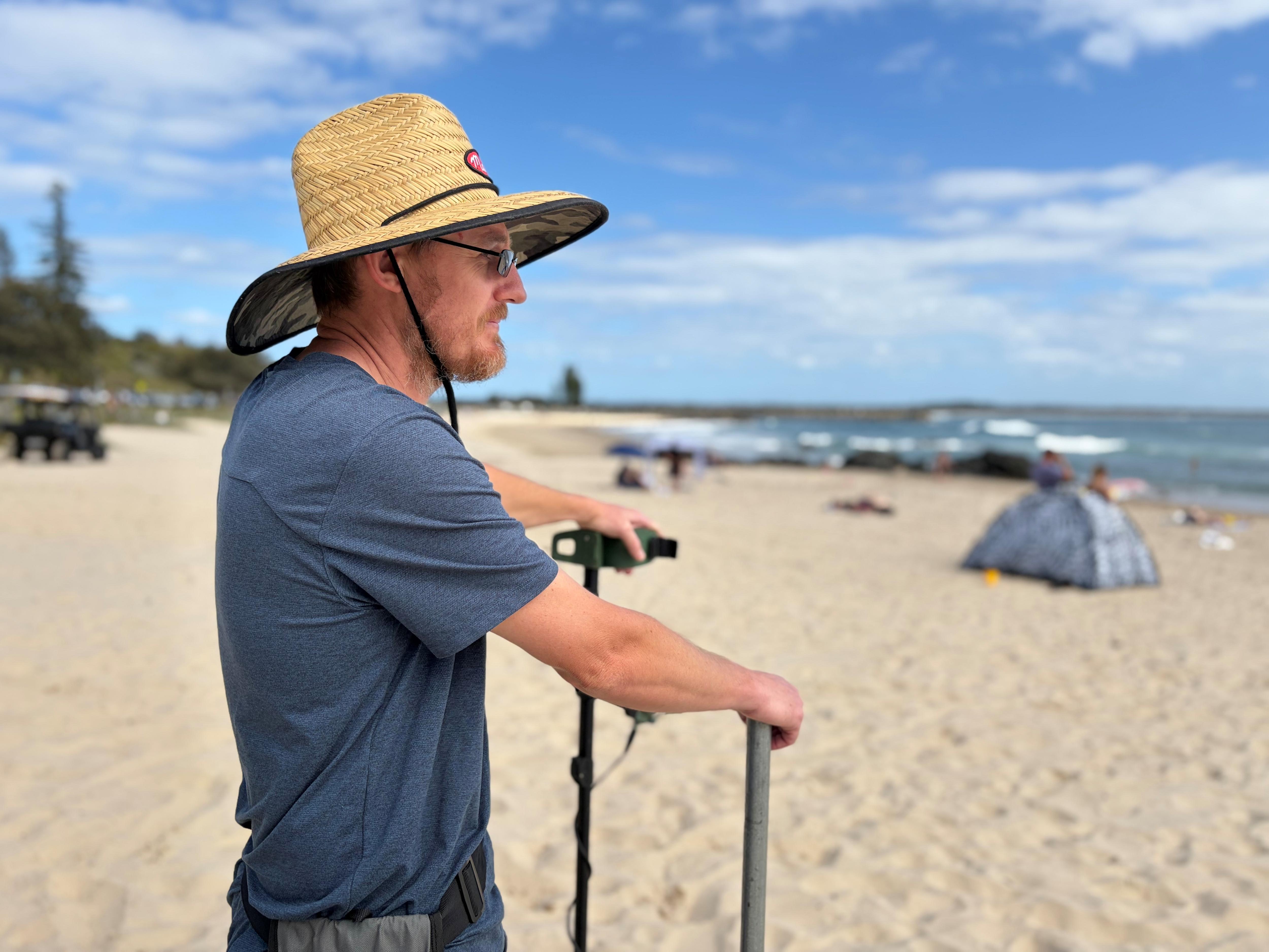 Um homem segurando um detector de metais olhando para o oceano, na praia.