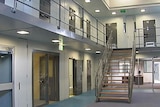 The interior of a prison with clean grey walls and see-through doors and metal stairs leading to a mezzanine.