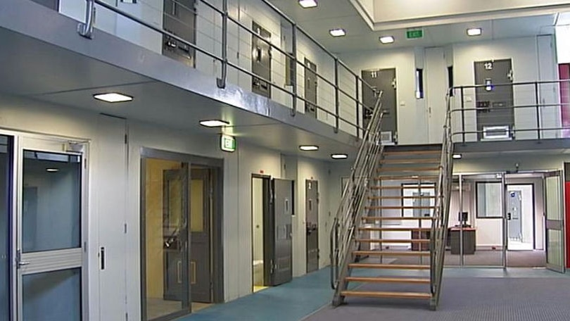 The interior of a prison with clean grey walls and see-through doors and metal stairs leading to a mezzanine.