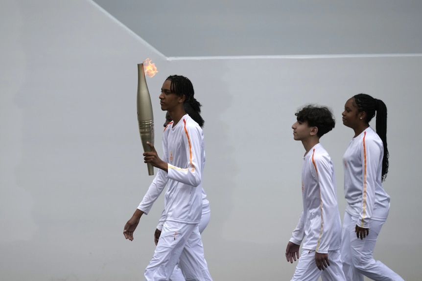 A group of youths dressed in white carry a large torch 