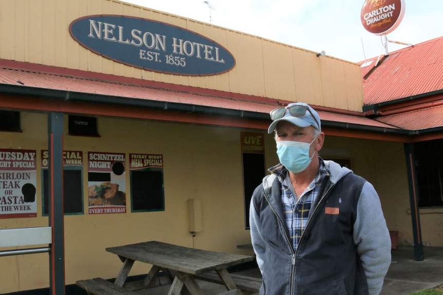 A man in a mask stands in front of a building with a sign reading "Nelson Hotel".