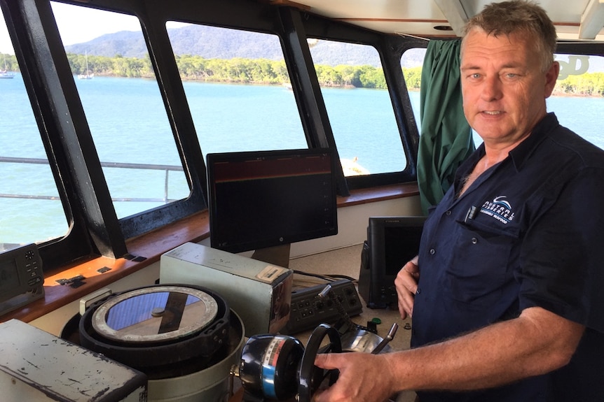 A skipper in the wheelhouse of a prawn trawler with the backdrop of the ocean, mangroves and mountains