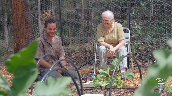 Older woman sitting in chair, smiling at young man kneeling at vegie garden bed