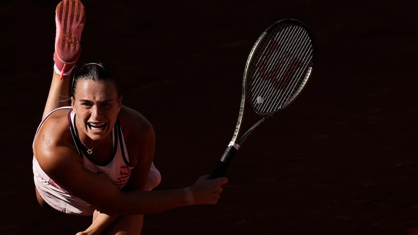 Woman hitting a tennis serve half in shadow. 