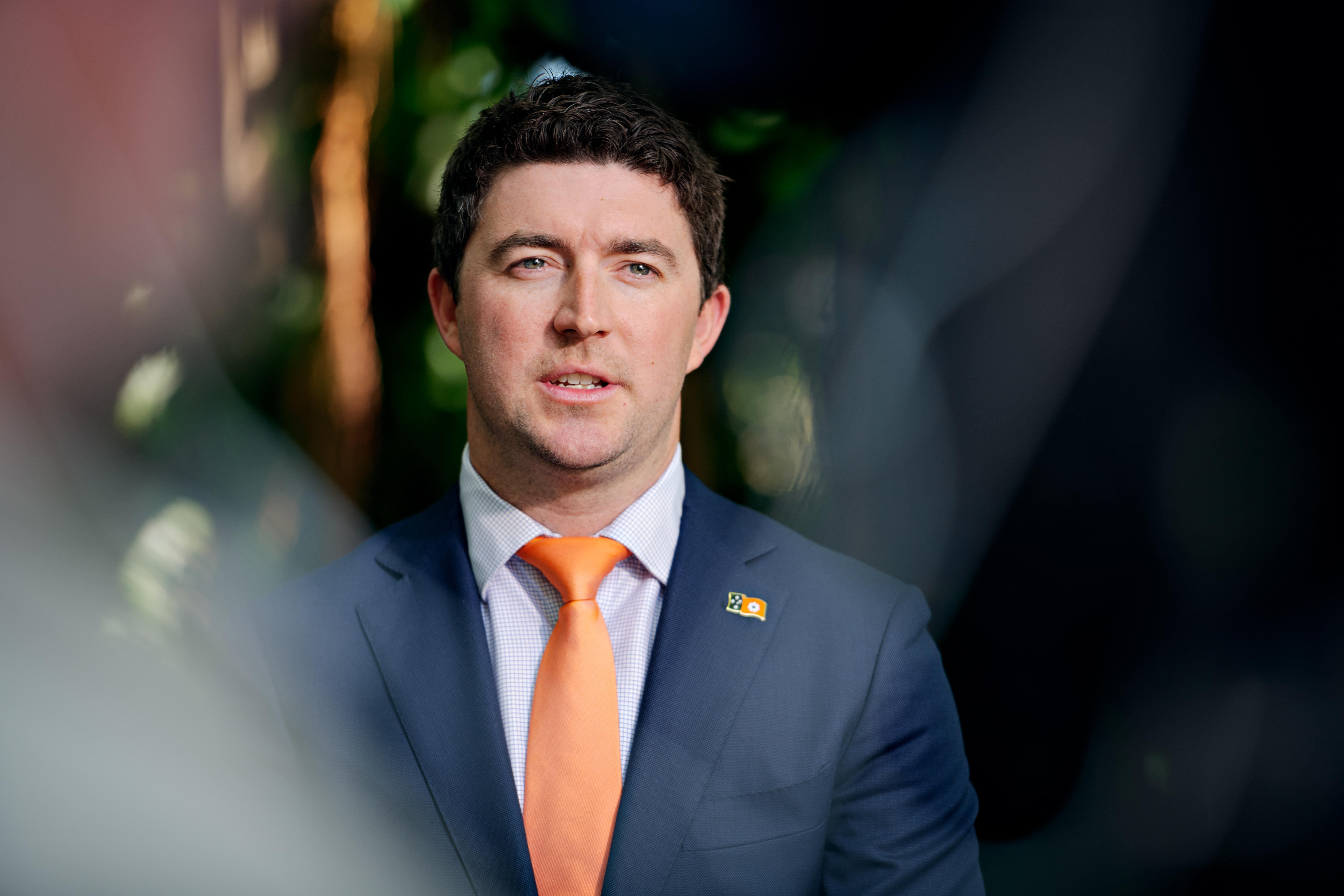 A man wearing a navy blue blazer and orange tie.