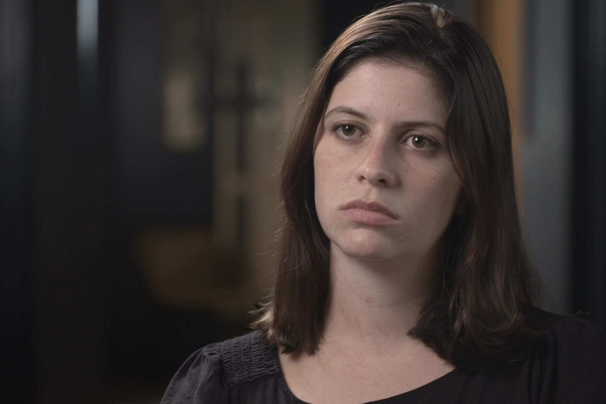 Woman with brown hair looks seriously at an interview.