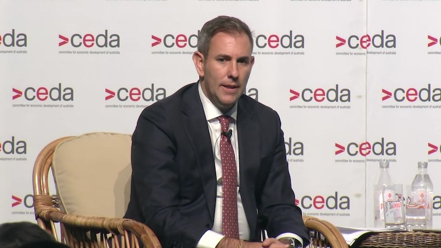 Treasurer Jim Chalmers sitting in a chair speaking on stage. A backdrop featuring the CEDA logo is behind him.