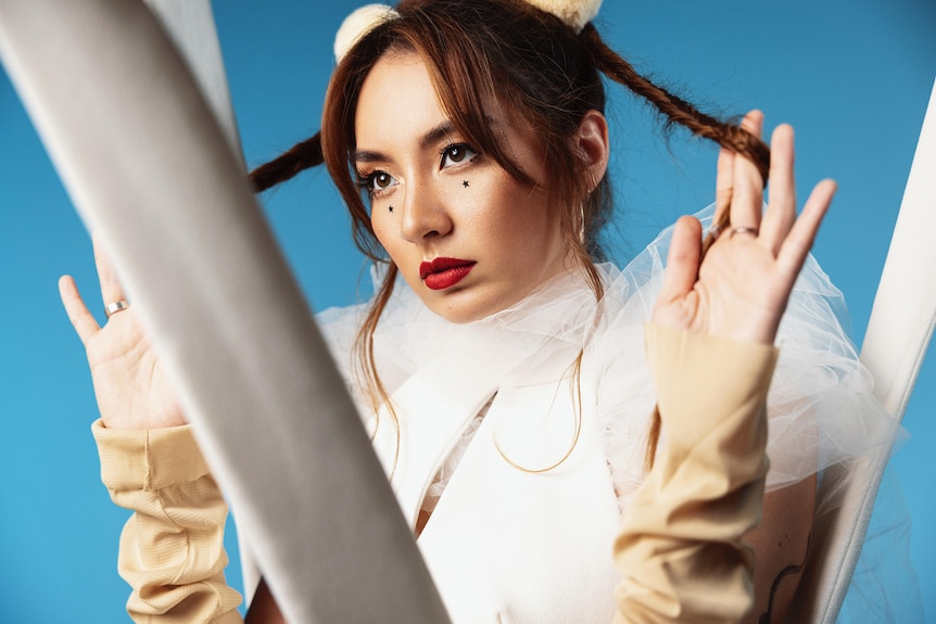 A performer stands twirling her hair through her fingers against a blue backdrop.