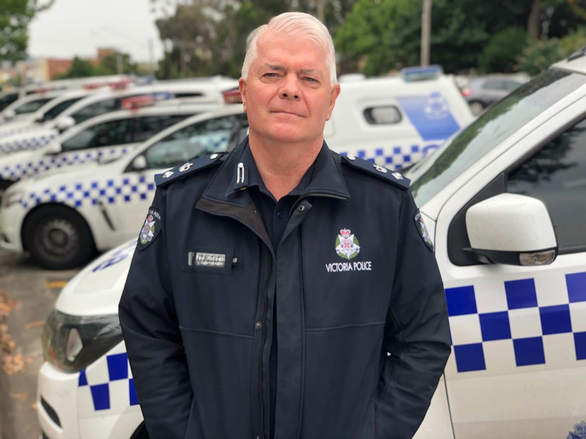 A police officer stands outside in front of a row of police cars.