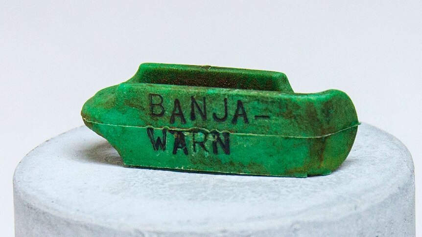 Small green sheep tag sitting on a white plinth engraved with the word "Banja-warn".