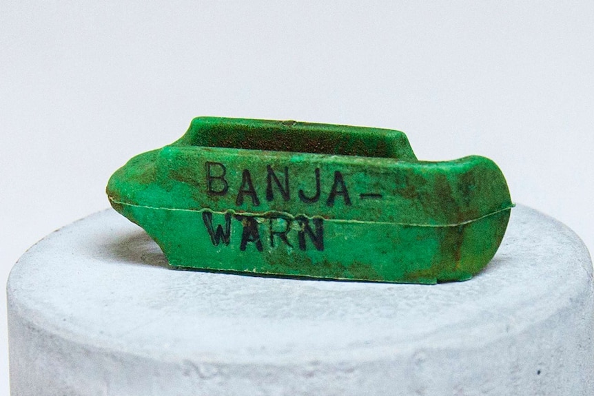 Small green sheep tag sitting on a white plinth engraved with the word "Banja-warn".