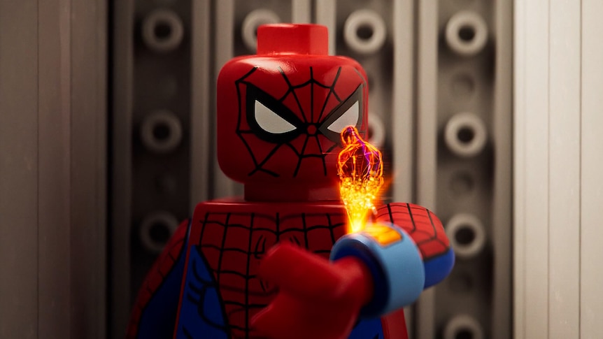 Still frame from Spider-Man movie showing a lego spider-man communicating with a hologram via a comms device on his wrist.
