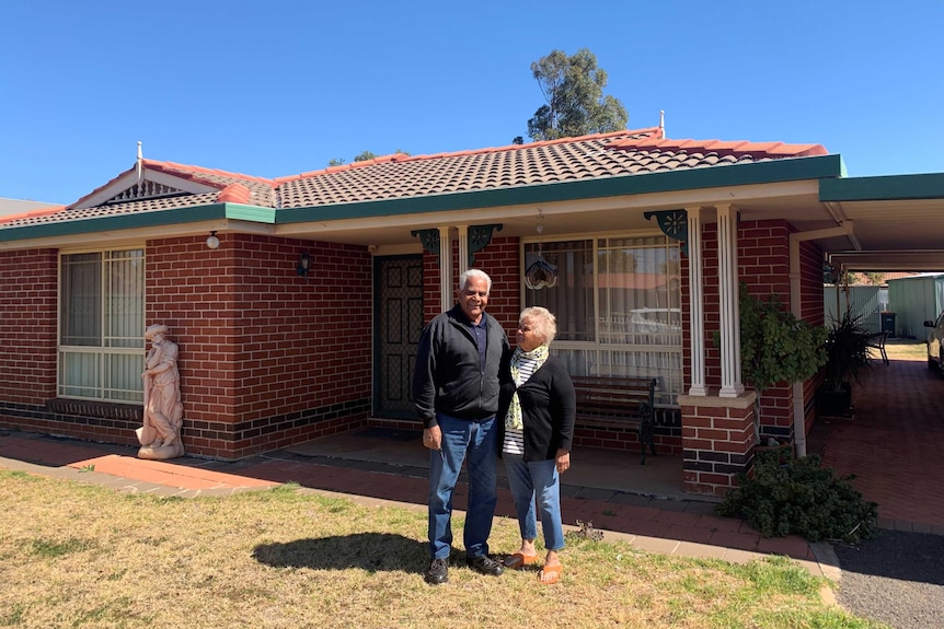 A man and a woman stand in the front yard of a red brick home