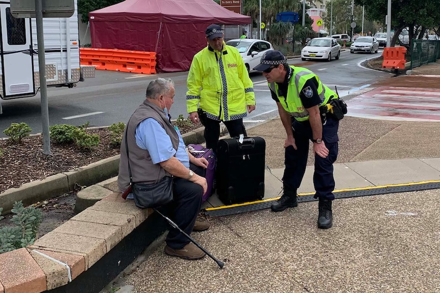 Police speaking to an elderly man sitting on the side of the road