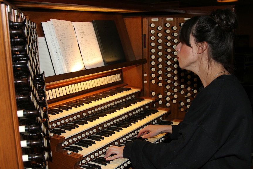 A woman looks at her notes while playing an organ.