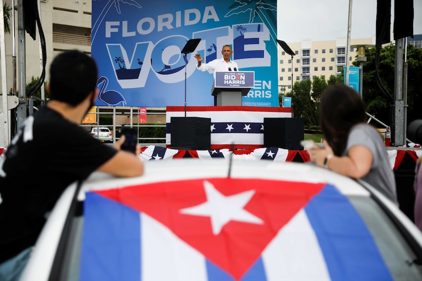 Barack Obama speaks in front of people in their cars at drive-in rally.