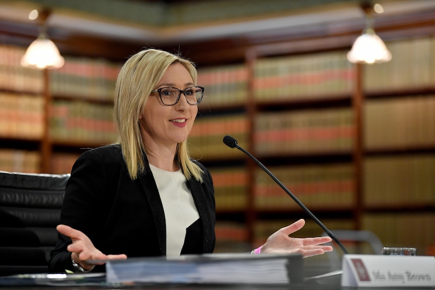 A woman with blonde hair and glasses smiles while sitting behind a microphone