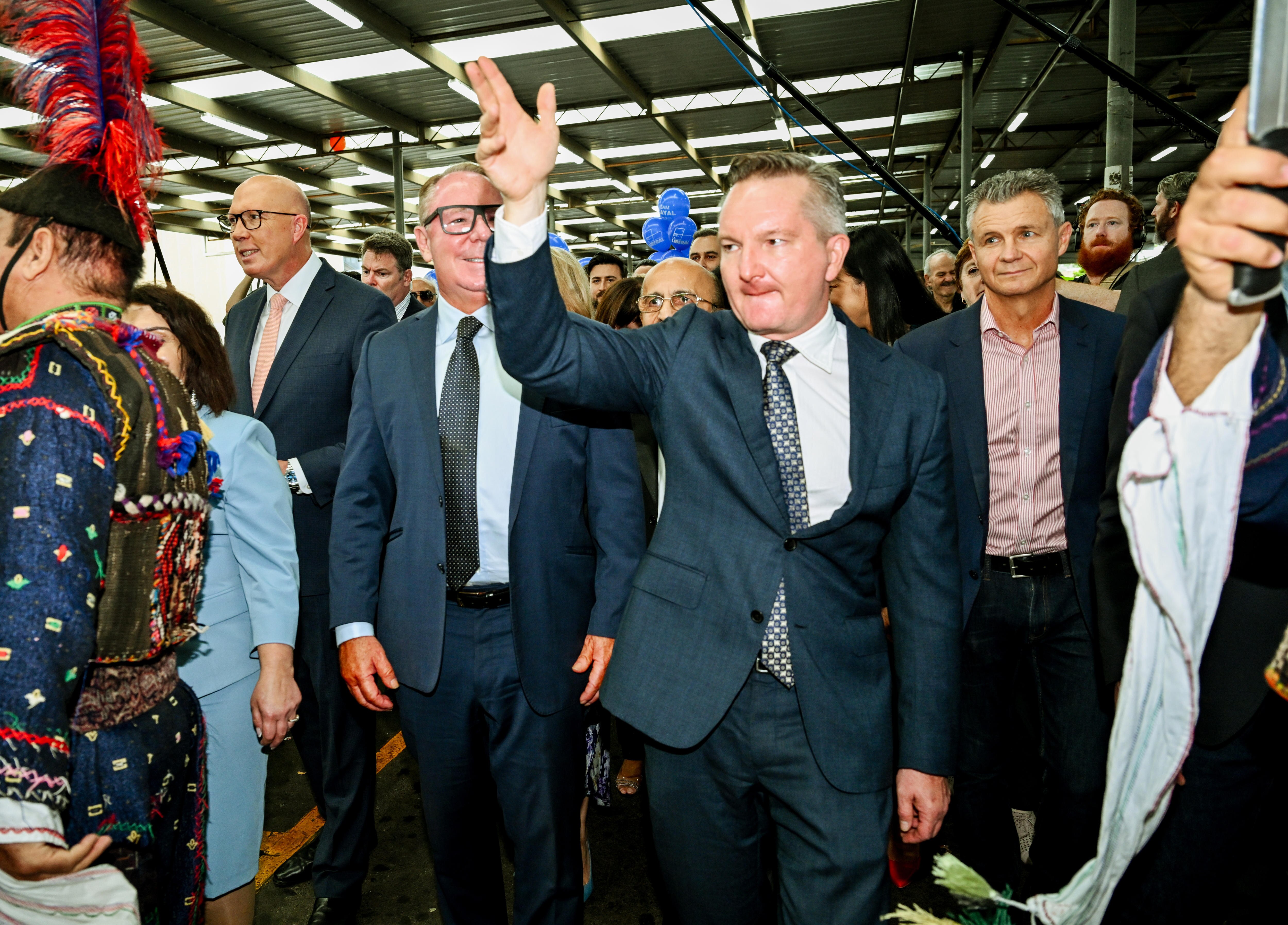 Chris Bowen walking with hand raised looks serious, Dutton smiling in background