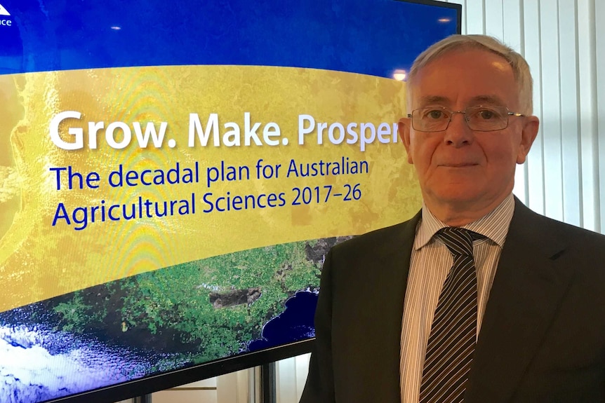 Dr Jeremy Burdon stands in front of signage reading: 'Grow. Make. Prosper: decadal plan for Australian agricultural sciences'