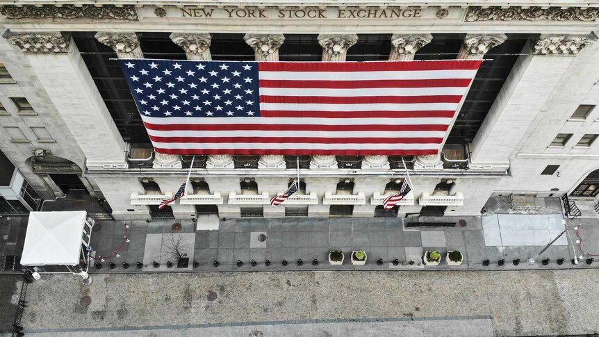 The New York Stock exchange with large american flag draping the front and an empty footpath during coronavirus lockdown