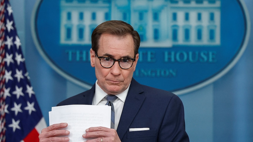 John Kirby shuffles papers at the podium in the white house press briefing room. 