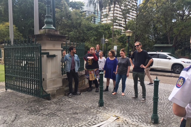 A group of six protesters stand at a gate at Parliament House in Brisbane.