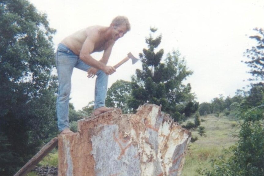 A man stands on top of a tree stump with an axe