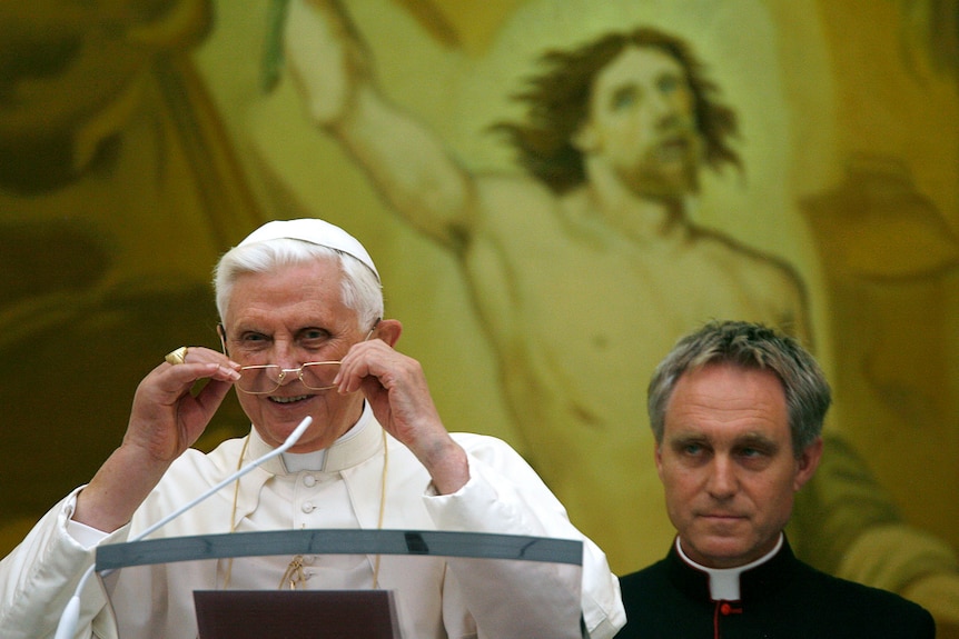 Pope Benedict XVI stands at a lectern while Georg Gaenswein stands behind him