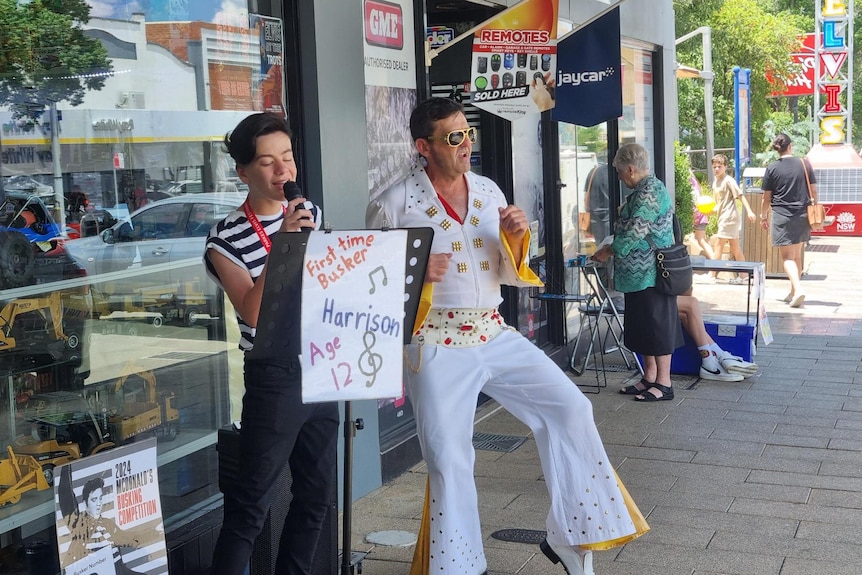 A boy bushing next to a man dressed up as Elvis in a white suit.