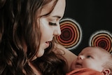 A smiling young woman, long brown curly hair, looks at baby in arms. Aboriginal dot painting circles on black behind them.
