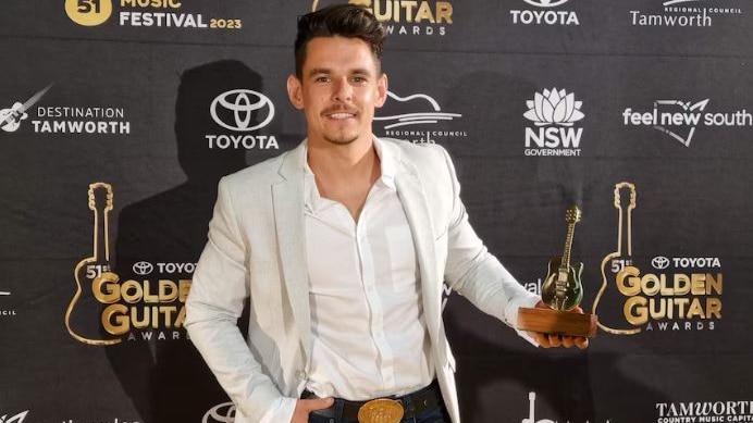 a young man holding a golden guitar award on a red carpet