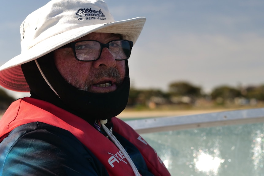 Close up of man wearing face covering, hat and glasses on a boat.