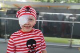 A child wearing a red and white striped pirate hat and shirt, medical eye patch covering her eye.