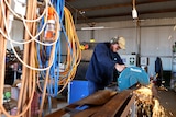 Chapman Valley farmer Brady Green welding in his farm shed with power cords in the foreground.