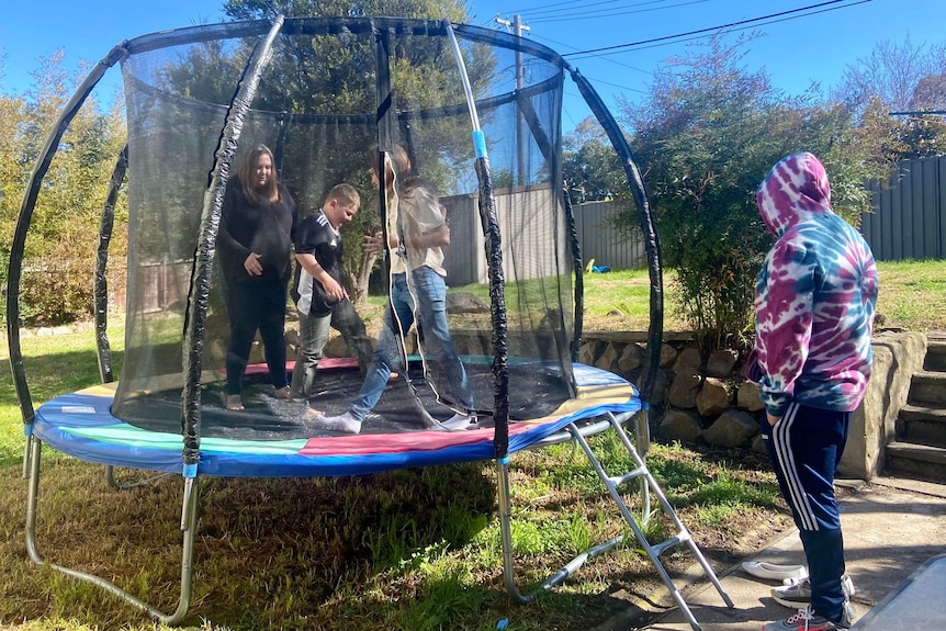 Children bouncing on a trampoline in the sun, with their Mother. 