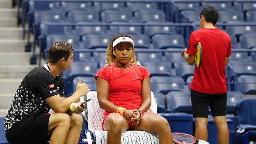 A female tennis player sits, slumped in her seat with her male coach talking to her.