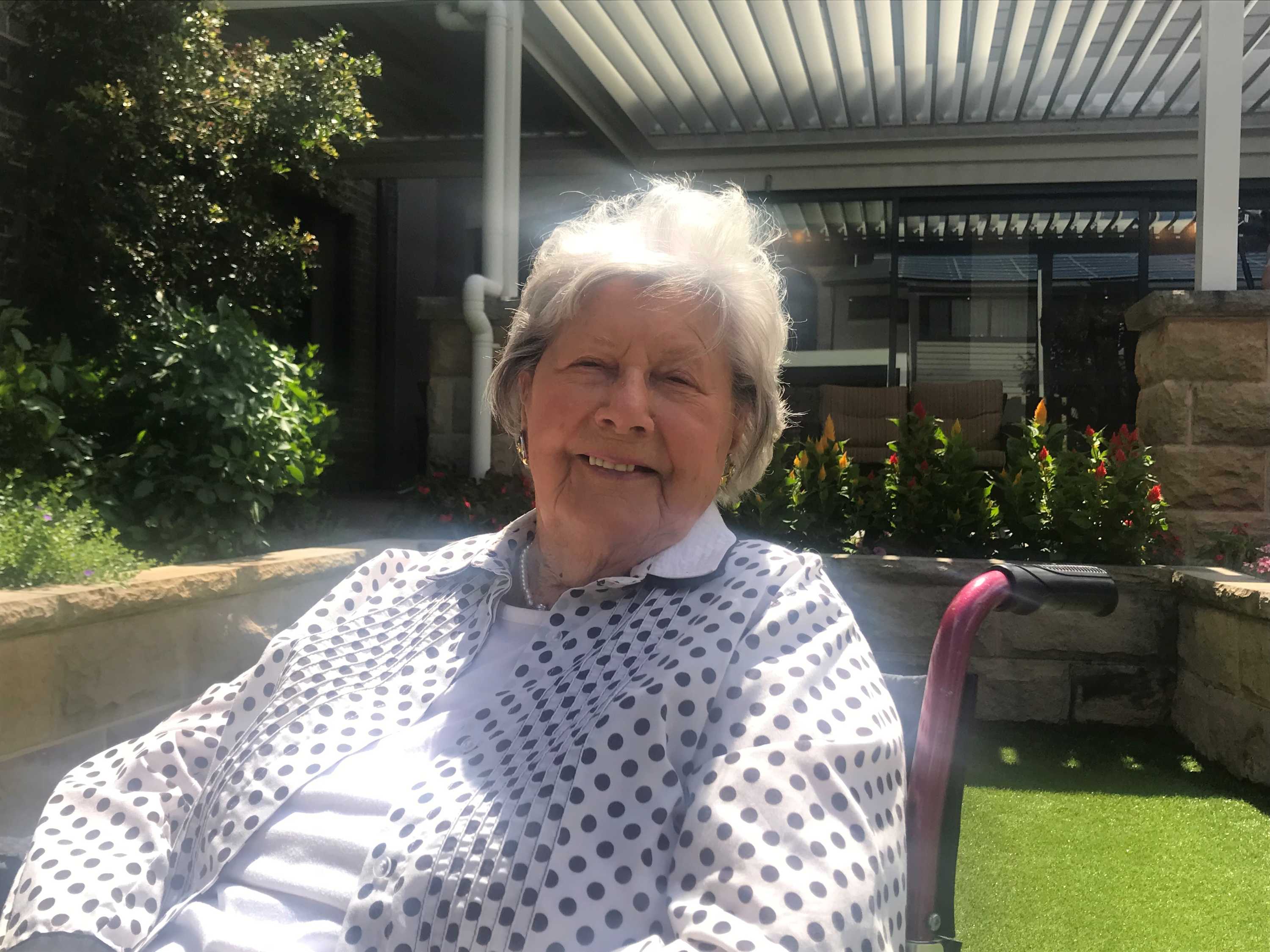 A woman with white hair sitting in a chair outside.