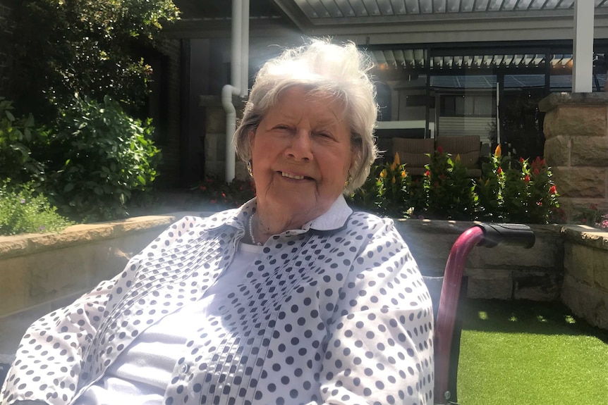 A woman with white hair sitting in a chair outside.