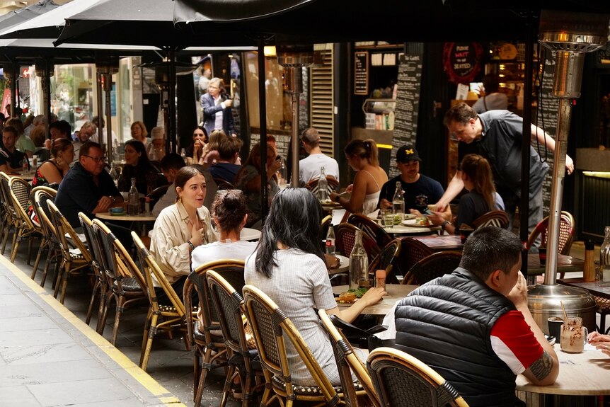 Many diners sit at cafe tables lining Degraves Street under umbrellas.