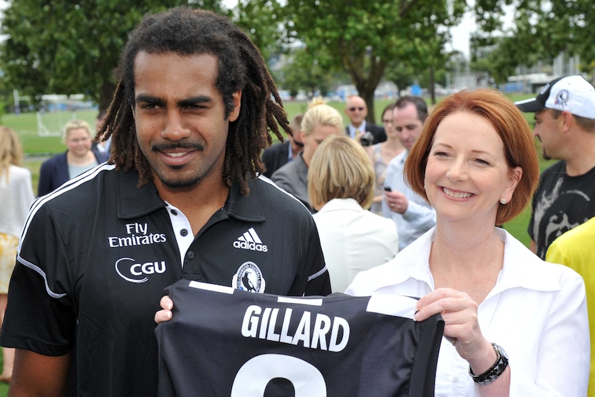 A football player presents the Prime Minister with a jersey, they hold it up and smile.