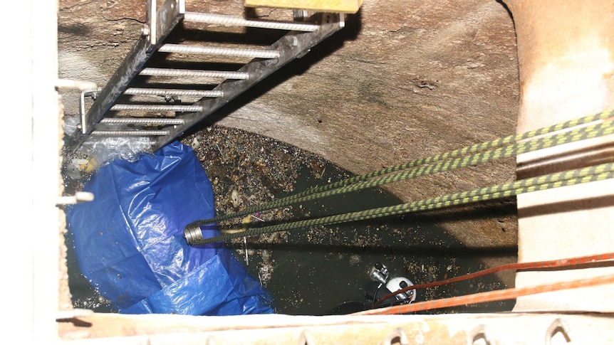 A blue body bag floats in a sewer.