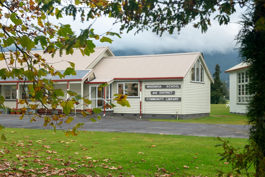 A small schoolhouse and library building is visible through the trees. 